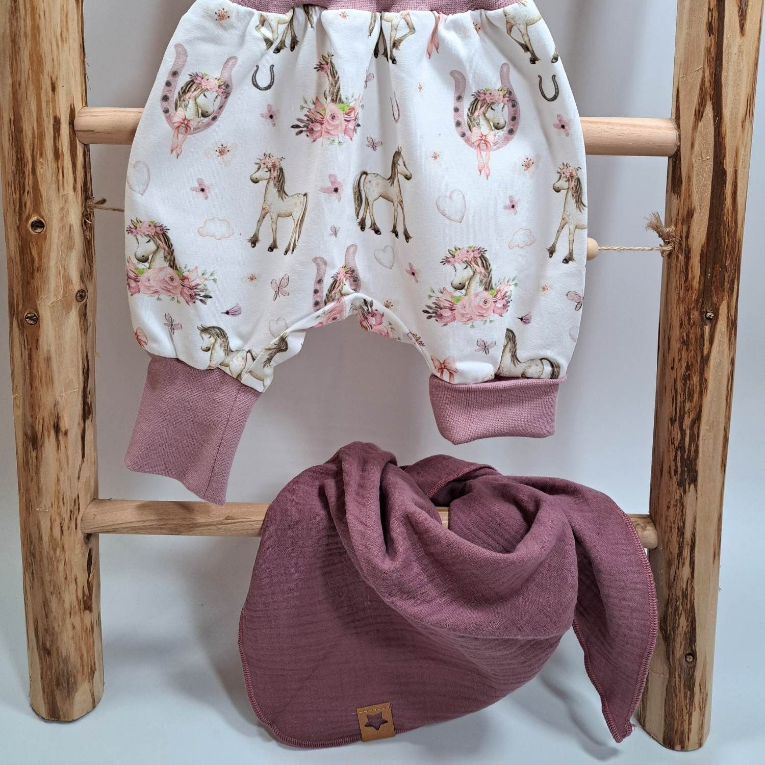 Mitwachsende Kleidung hier am Beispiel der langen Pumphose "Boho Pferde". Das linke Beinbündchen ist umgeschlagen. Und am Beispiel eines einlagigen Musselintuches in altrosa, das durch den Knoten variabel in der Größe ist.